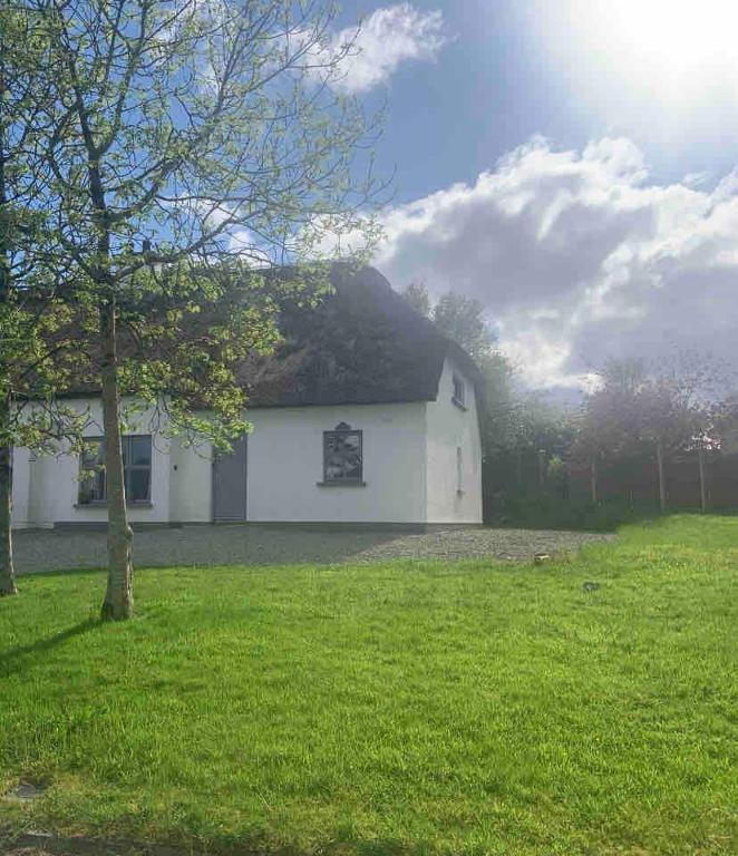 a white barn with a thatched roof in a field at Fionas thatched cottage eile in Killarney