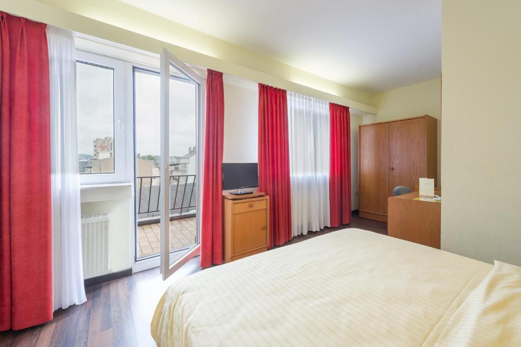 een slaapkamer met rode gordijnen en een bed en een balkon bij Logis Hôtel Acacia in Esch-sur-Alzette