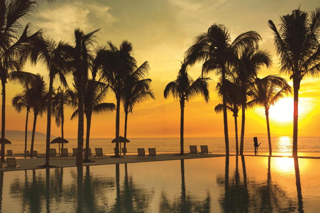 a person walking on a beach with palm trees at Secrets Vallarta Bay Resort & SPA - Adults Only in Puerto Vallarta