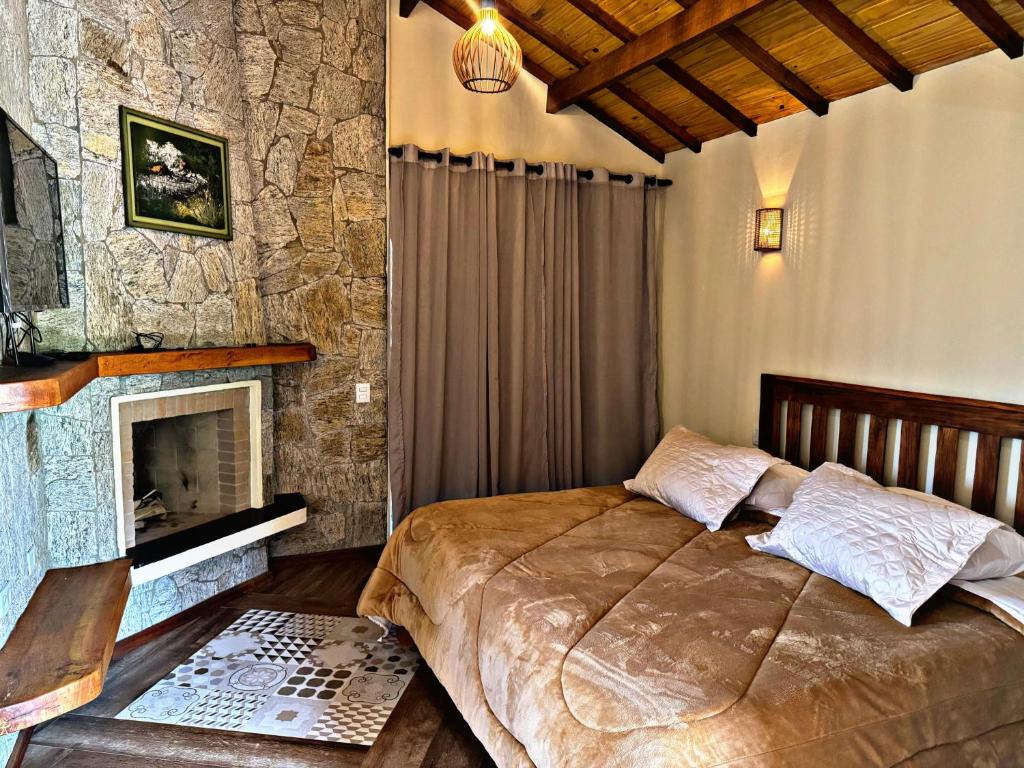 Chalés Recanto Vista do Valle في مونتي فيردي: غرفة نوم مع سرير ومدفأة حجرية