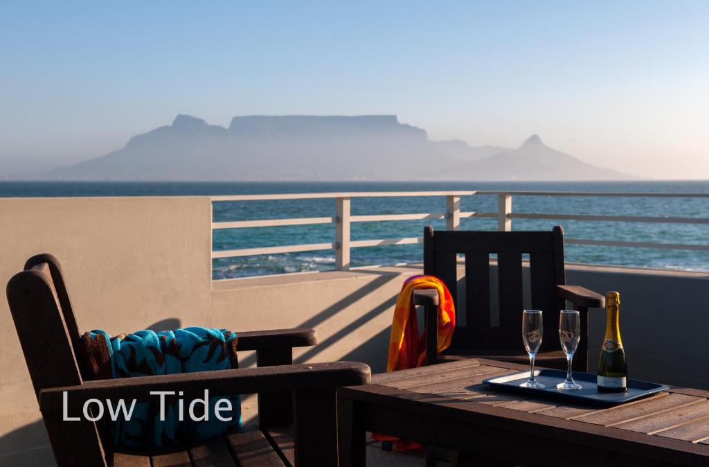 a wooden table with two wine glasses and a view of the ocean at Bokkombaai in Bloubergstrand