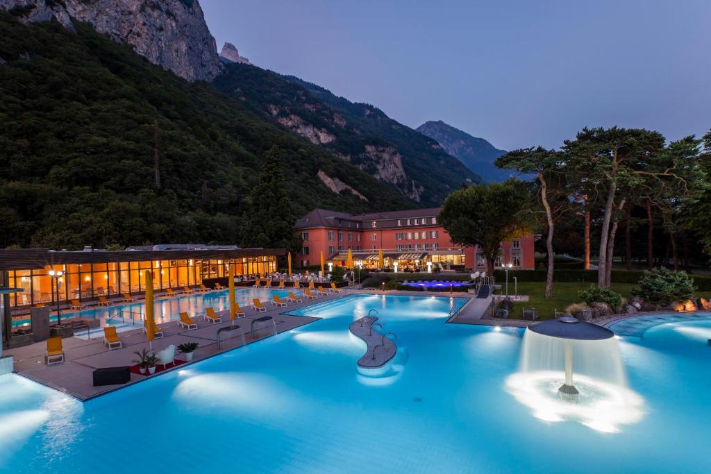 a resort with a blue pool with mountains in the background at Grand Hotel des Bains in Lavey-les-Bains