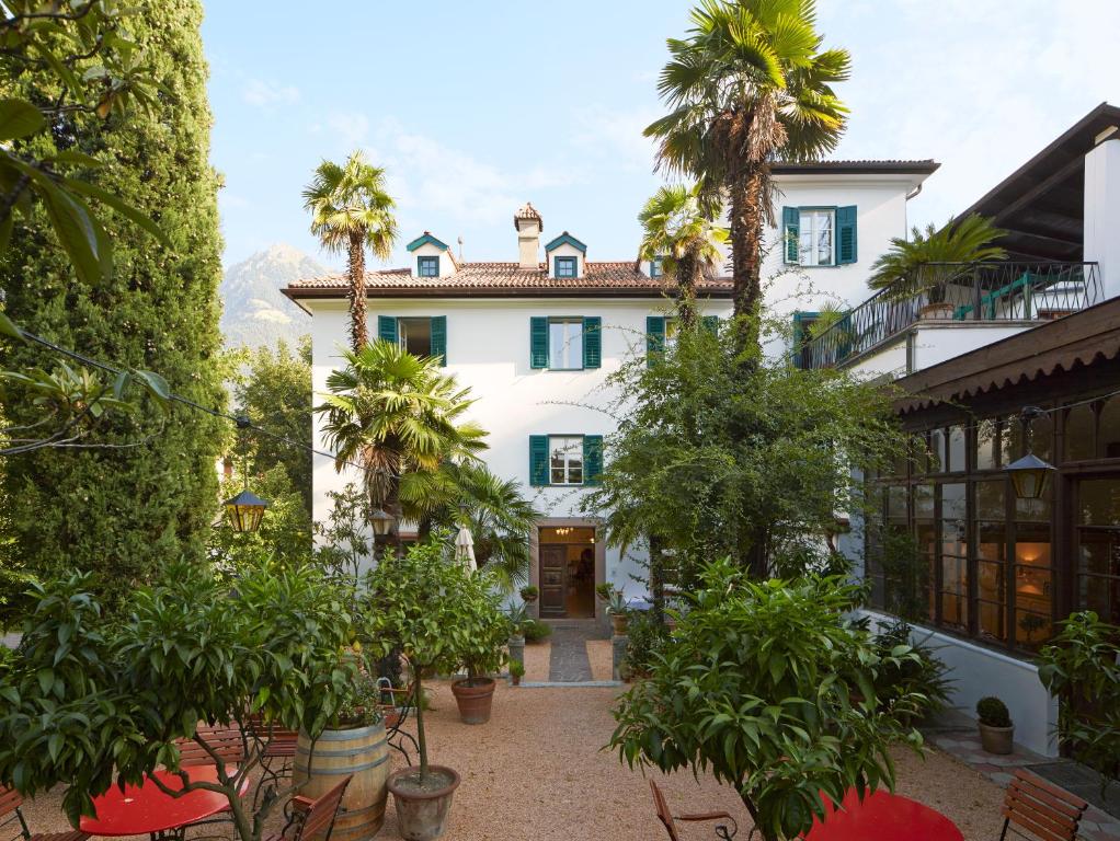 uma vista exterior de uma casa branca com palmeiras em Ottmanngut Suite and Breakfast em Merano