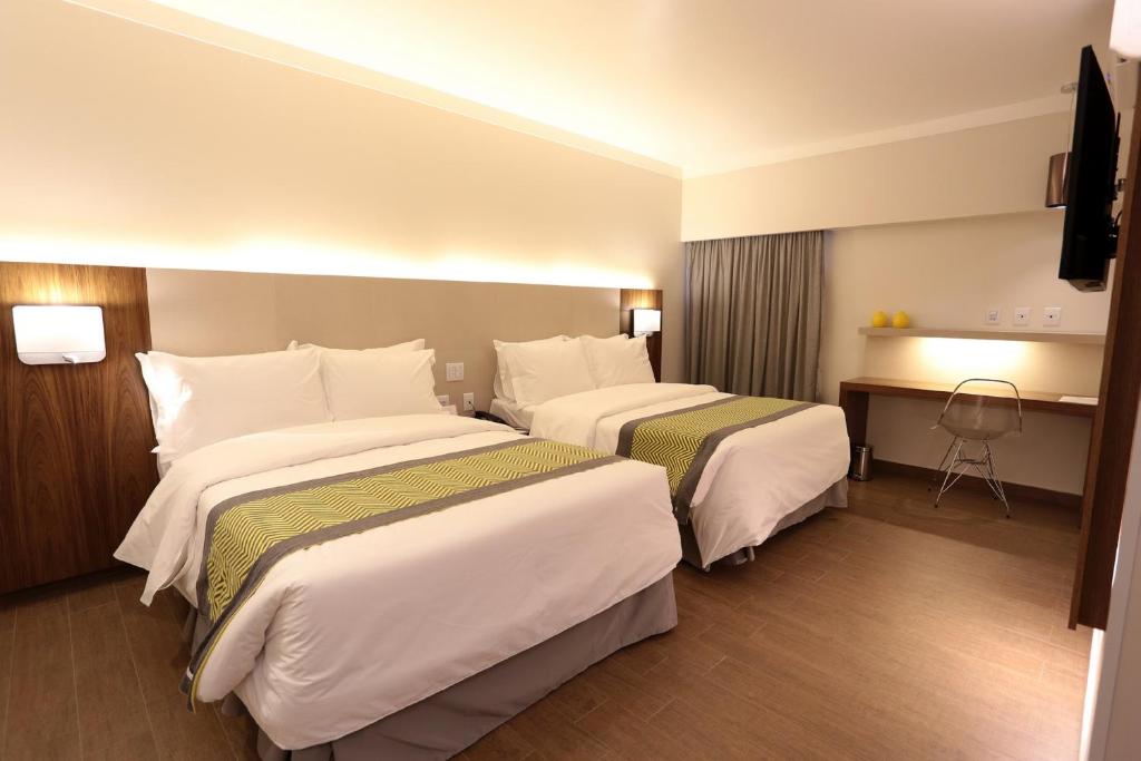 a hotel room with two beds and a desk at Oasis Plaza Hotel in Ribeirão Preto