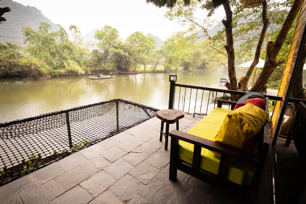 a bench sitting on a balcony next to a river at Trang An Ecolodge in Ninh Binh