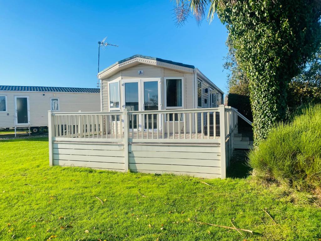 a white house with a porch and a fence at Stylish Inviting 2 Bedroom Caravan with Sea View in East Mersea