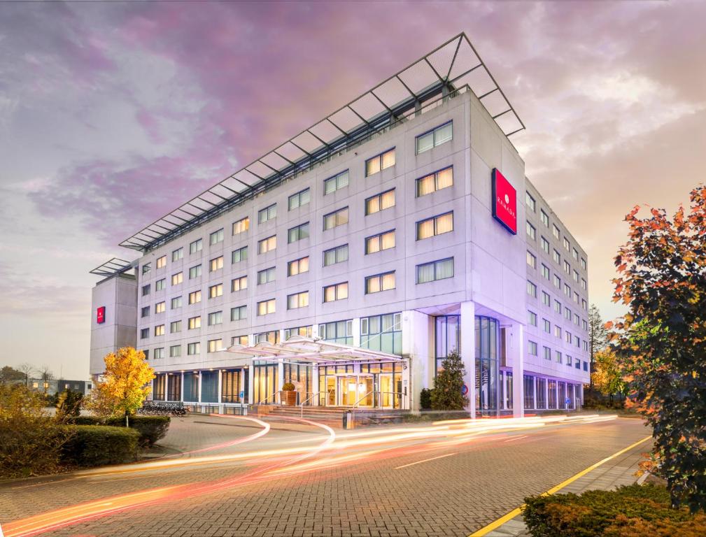 バドフーフェドルプにあるRamada by Wyndham Amsterdam Airport Schipholの赤い看板が立つ白い大きな建物