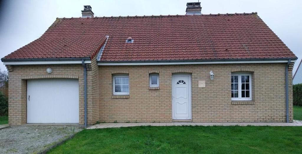 a brown brick house with a white garage at Les Rolliannes Maison au village in Surques