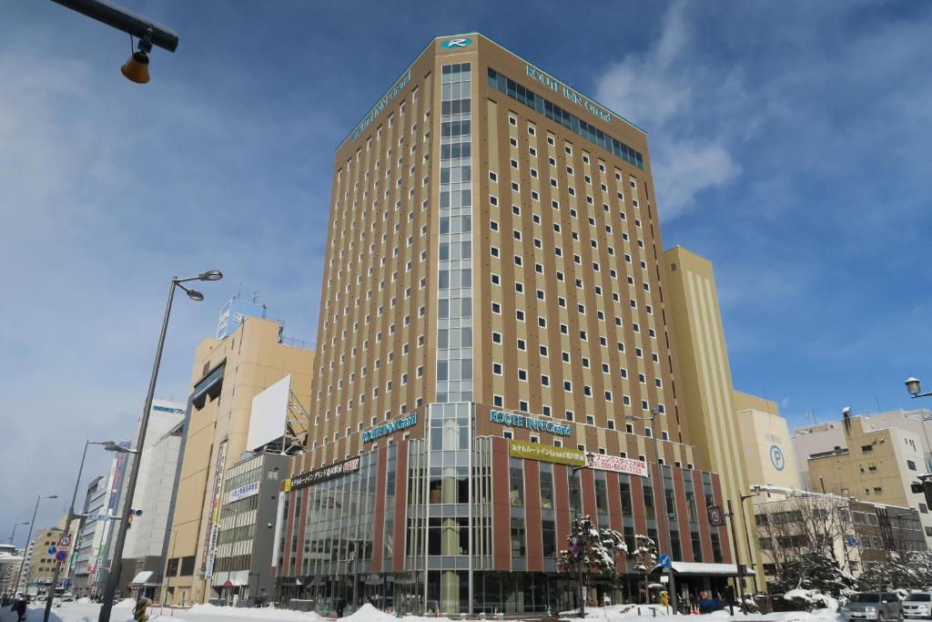 a tall building in a city with snow on the ground at Hotel Route Inn Grand Asahikawa Ekimae in Asahikawa