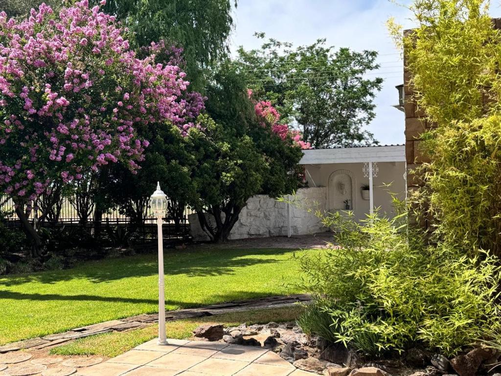 Green Acres Farm Cottage في Ritchie: ساحة بها منزل به ورد وردي واضاءة الشارع