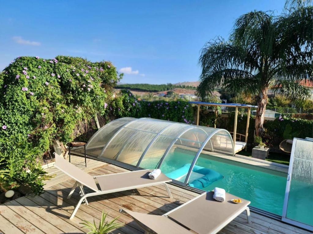 a swimming pool with two chairs and a glass house at ברוגע אצל נוגה סוויטה עם בריכה פרטית in Moshav Ramot