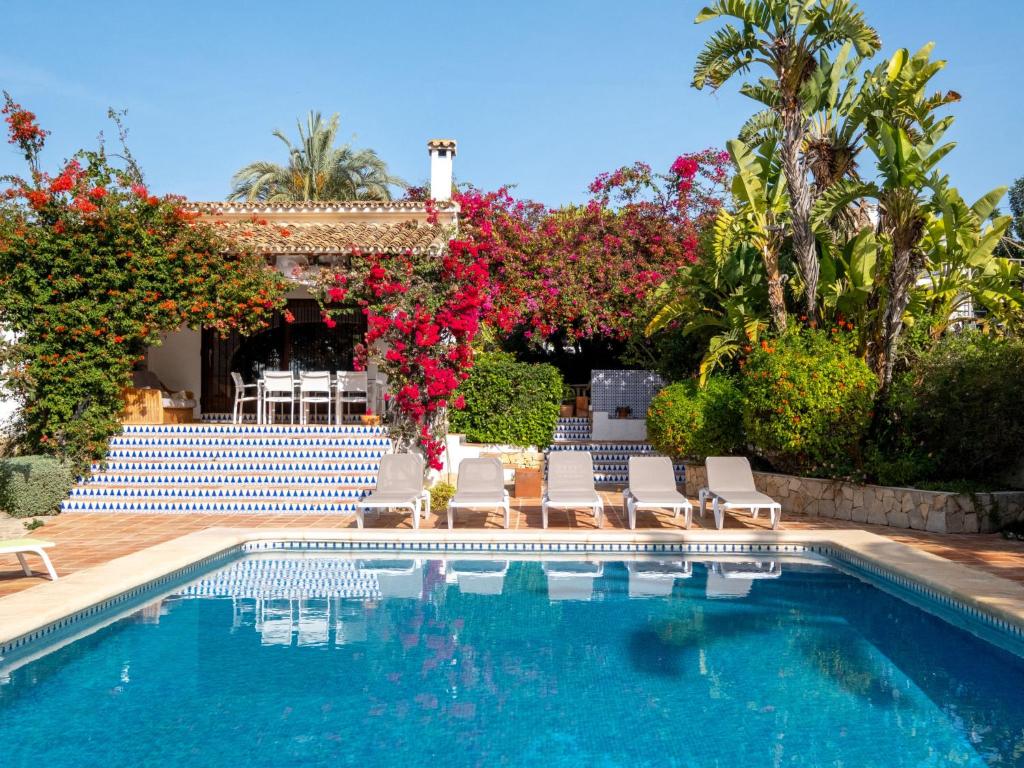 a swimming pool with chairs and flowers next to a house at Villa La Familia by Interhome in Benissa