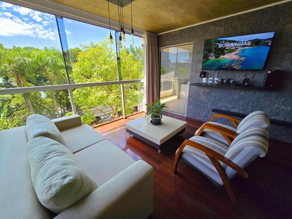 a living room with a white couch and a large window at Refúgio da Lagoinha - Centro de Bombinhas in Bombinhas