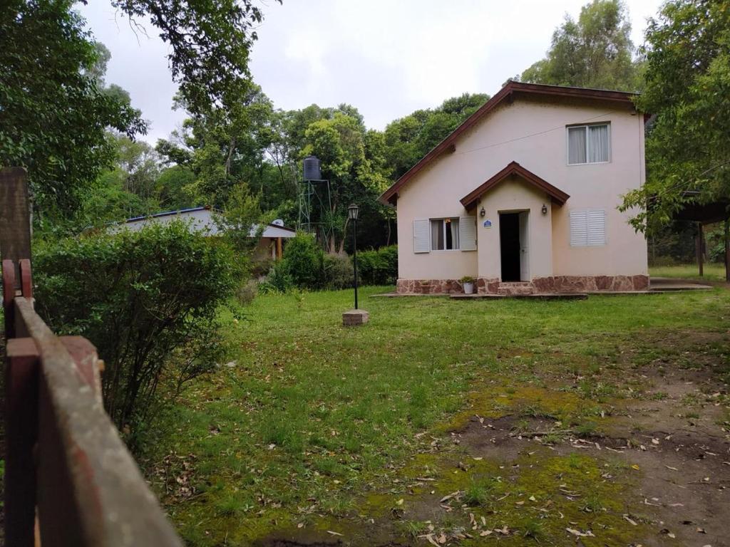 a small white house in a yard with a fence at Cabaña Villa Ciudad Parque los Reartes in Villa Ciudad Parque