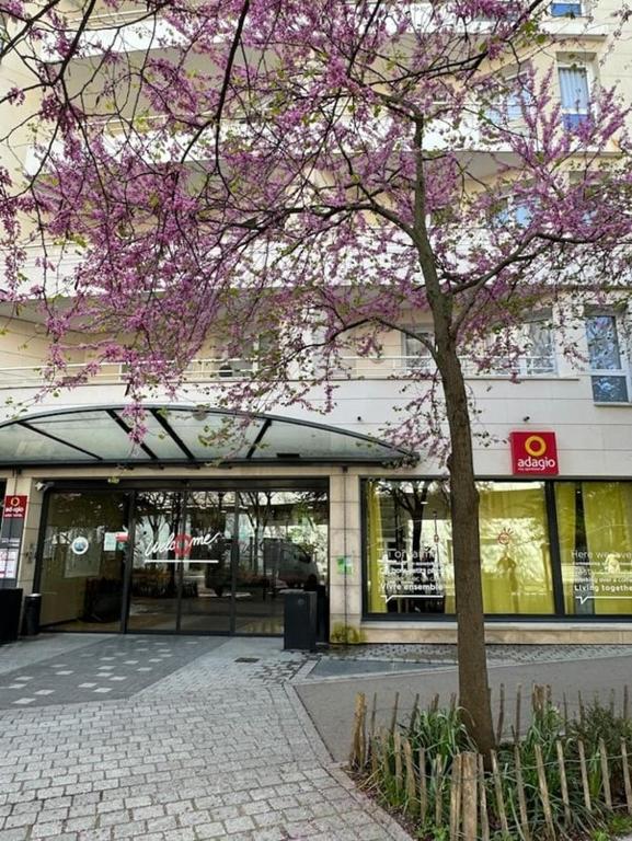 un arbre aux fleurs roses devant un bâtiment dans l'établissement ApparthotelParisDefenseArenaElyseeEiffel, à Courbevoie