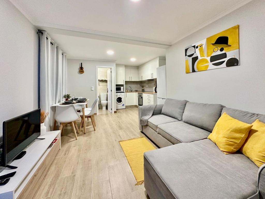a living room with a gray couch and a kitchen at Casa do Perestrelo - Guest House in Machico