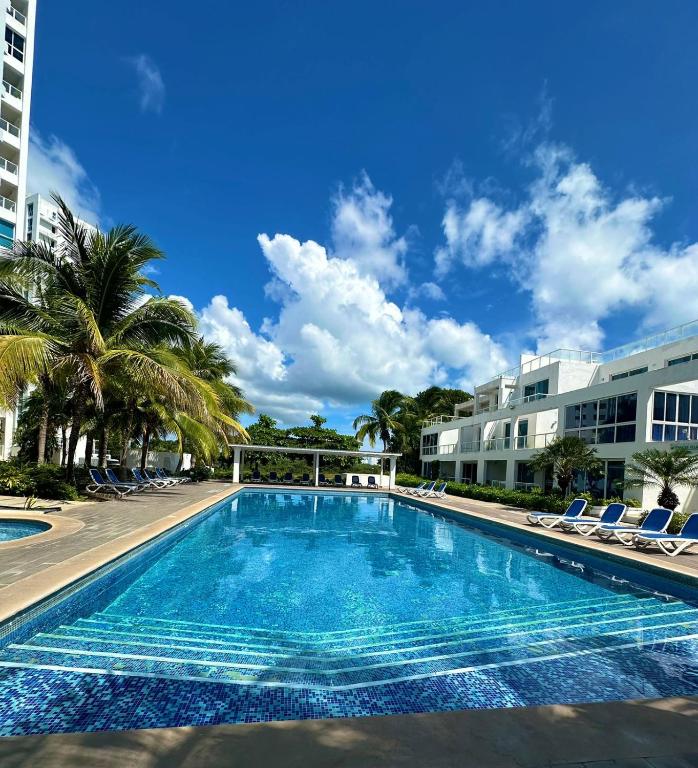 a swimming pool with chairs and palm trees and a building at Villas del Mar PTY in Río Hato