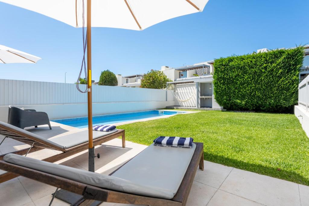 a patio with an umbrella and chairs and a pool at Villa Oliveira in Sesimbra