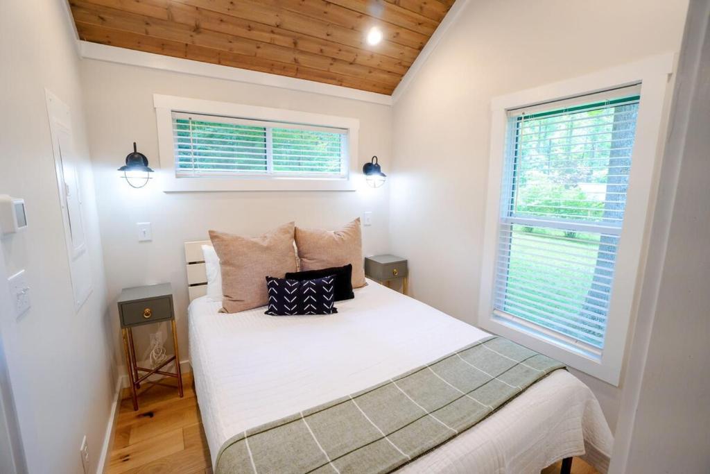 a small bedroom with a white bed with two windows at Tiny home Fire Pit Fishing Pond BBQ Sage Cabin in Gatlinburg