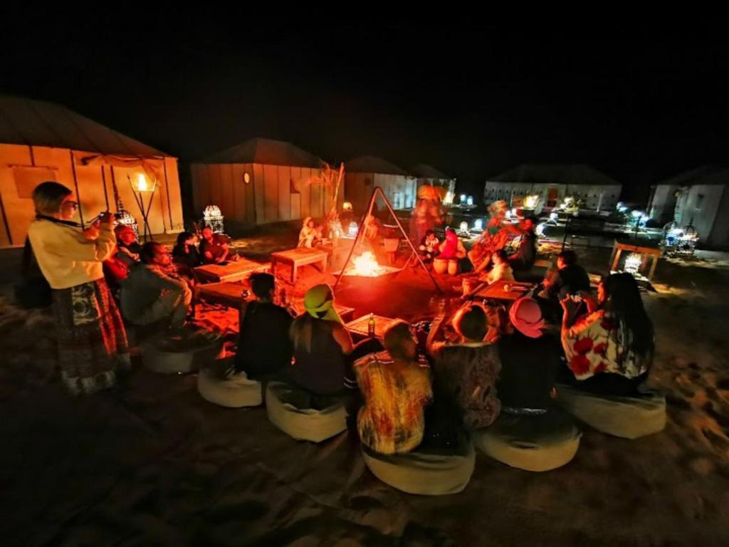 a group of people sitting around a table at night at Merzouga Desert Campsite &Activities in Merzouga