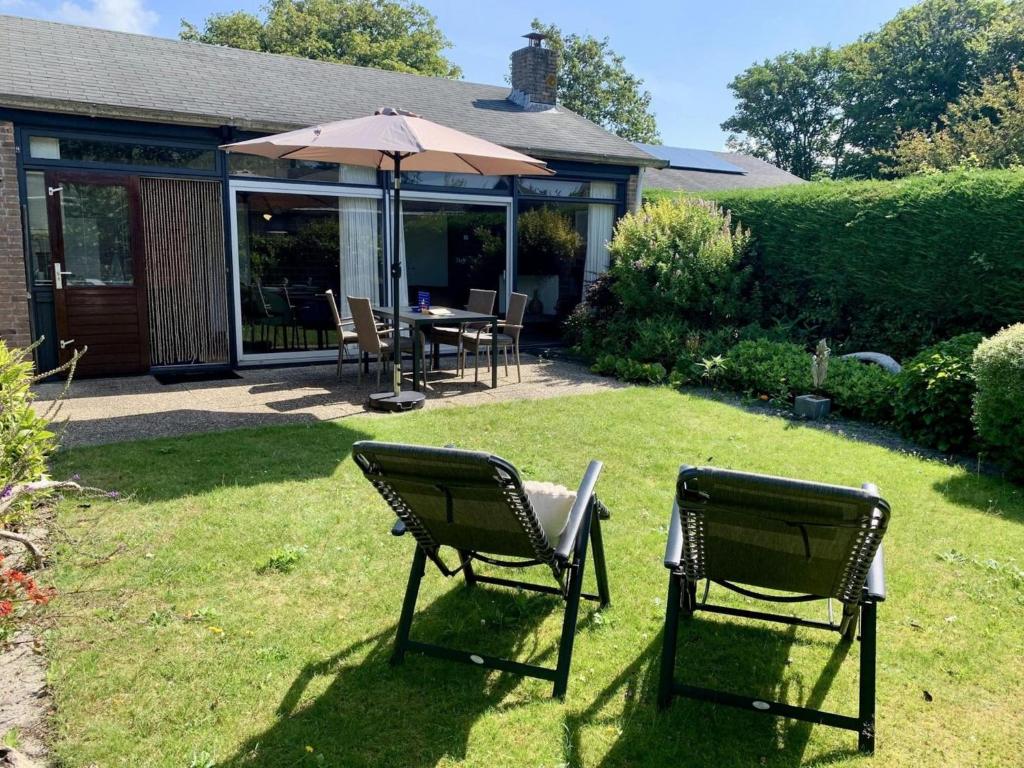 two lawn chairs and an umbrella in a yard at Bungalow in dune area of Sint Maartenszee in Sint Maartenszee