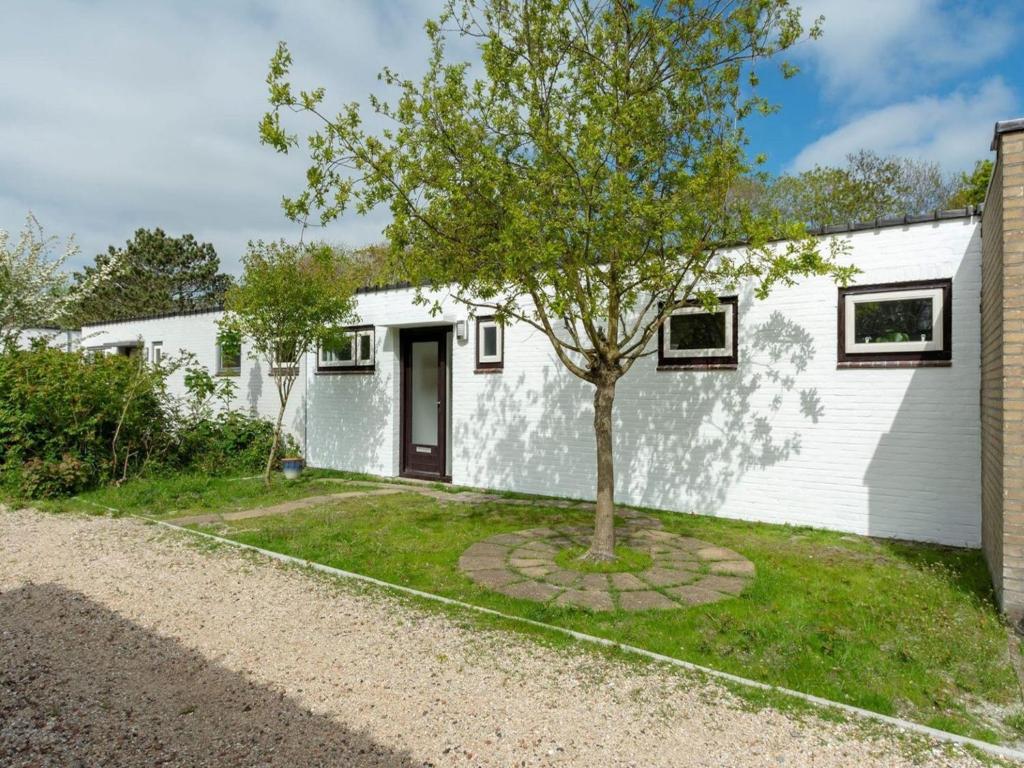 a white house with a tree in the yard at Furnished bungalow near beach in Sint Maartenszee