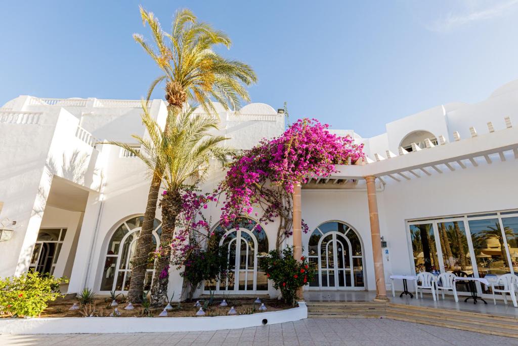 a white building with palm trees and purple flowers at Iris Hotel & Thalasso in Taguermess