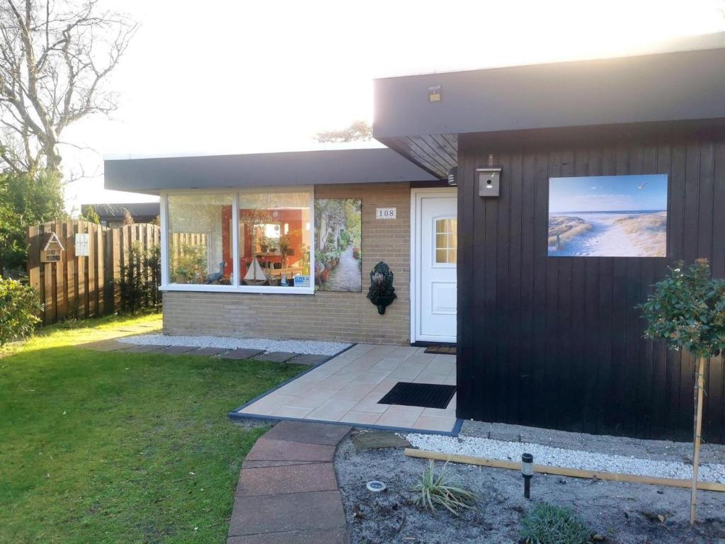 a small house with a white door and a yard at Inviting bungalow with private garden in Sint Maartenszee