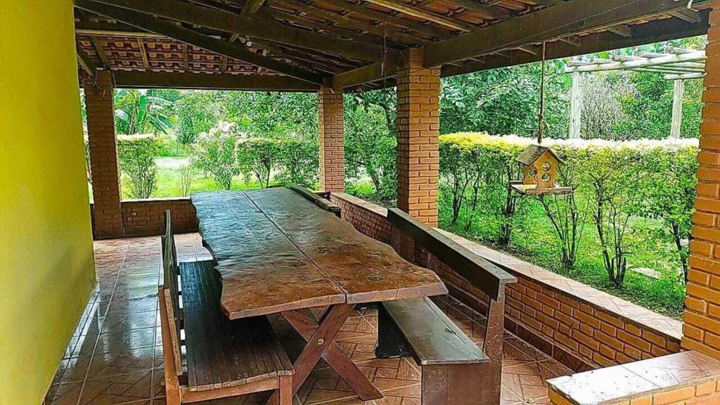 a wooden table on a patio with a large window at Recanto Sol Maior - Casa Girassol in Sapucaí-Mirim