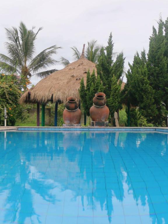 a swimming pool with two large vases next to a hut at Famoris Cottages in Tetebatu
