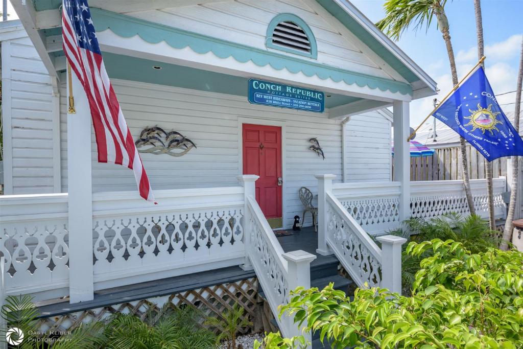 a white house with a red door and a flag at Porchside Paradise Conch Republic Cottage in Key West