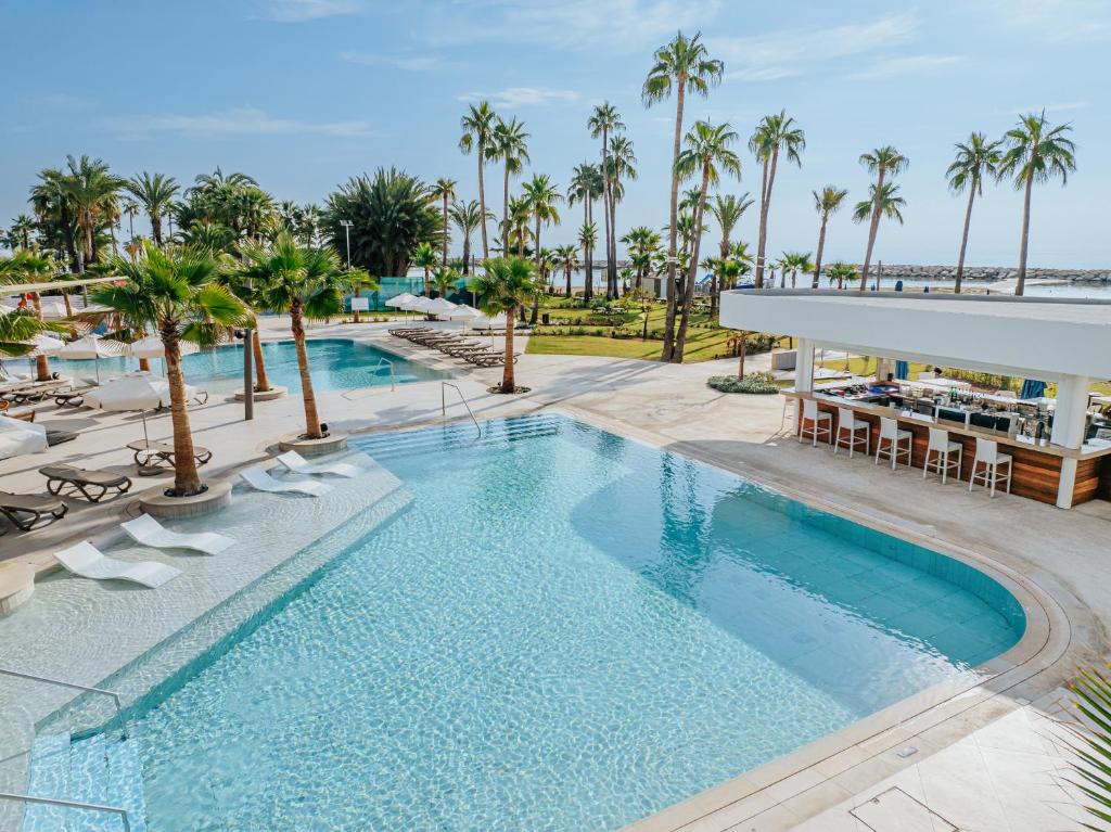 a pool at a resort with chairs and palm trees at Lordos Beach Hotel & Spa in Larnaca