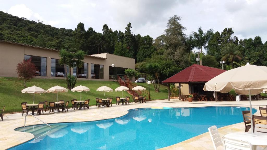einen Pool mit Tischen, Stühlen und Sonnenschirmen in der Unterkunft Hotel Nascentes da Serra in Poços de Caldas