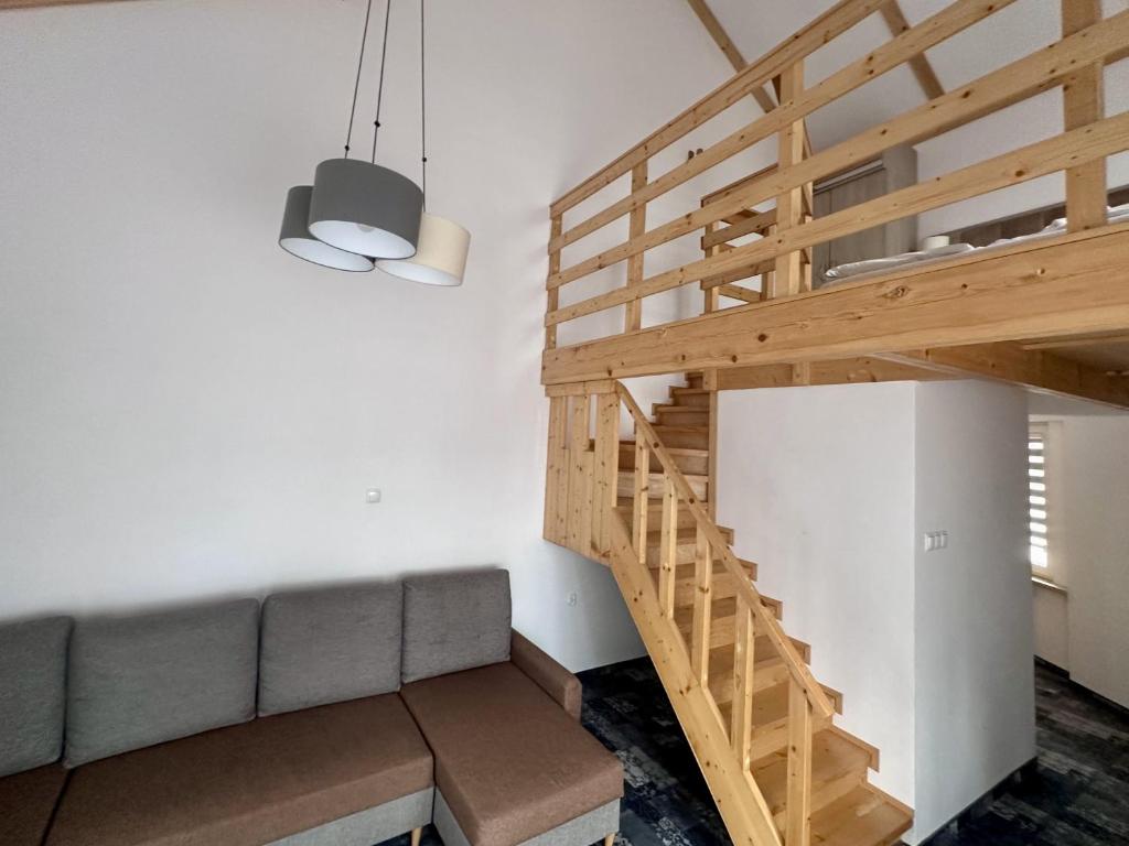 Open-plan loft with wooden staircase and mezzanine, gray sectional sofa, modern pendant lights.
