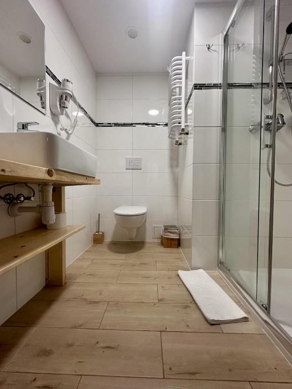 Bright compact bathroom with wooden floor, wall-mounted toilet, glass shower, sink, towel radiator.