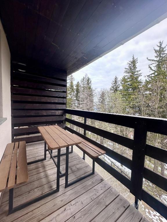 Covered wooden balcony with picnic table and benches overlooking evergreen trees and cloudy sky.