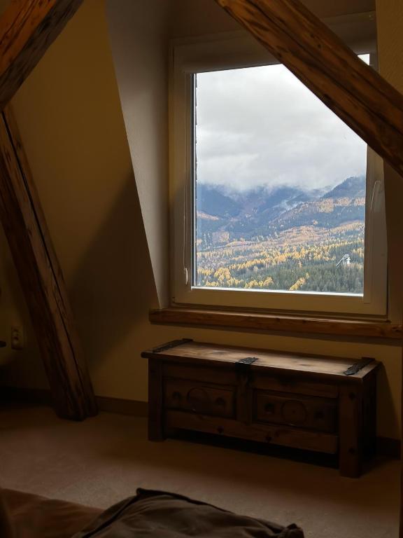 Small window framing mountain view above a rustic wooden chest, angled beams surrounding the alcove