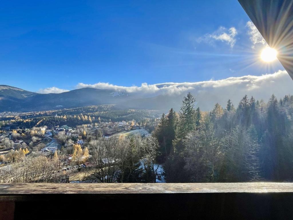 Sunburst over mountain valley and village, pine forest below seen from wooden balcony.