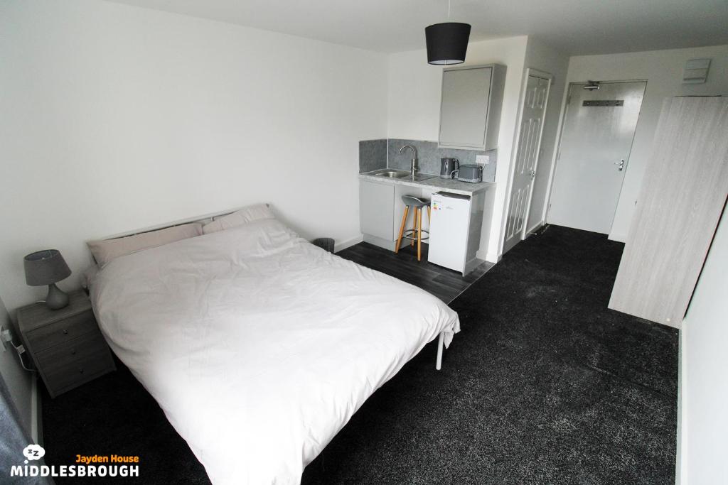 a bedroom with a white bed and a small kitchen at Jayden House in Middlesbrough