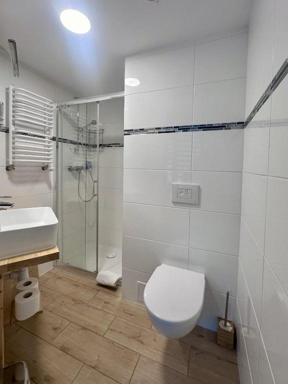 Modern white-tiled bathroom with glass shower, wall-mounted toilet and wooden-style flooring.
