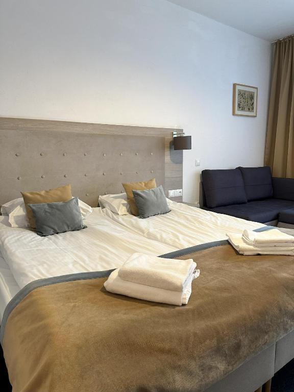 Bright twin beds with tufted headboard, folded towels, small dark sofa in cozy room.