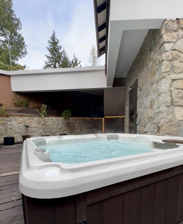 Outdoor bubbling hot tub on wooden deck beside a stone wall under a sheltered overhang.