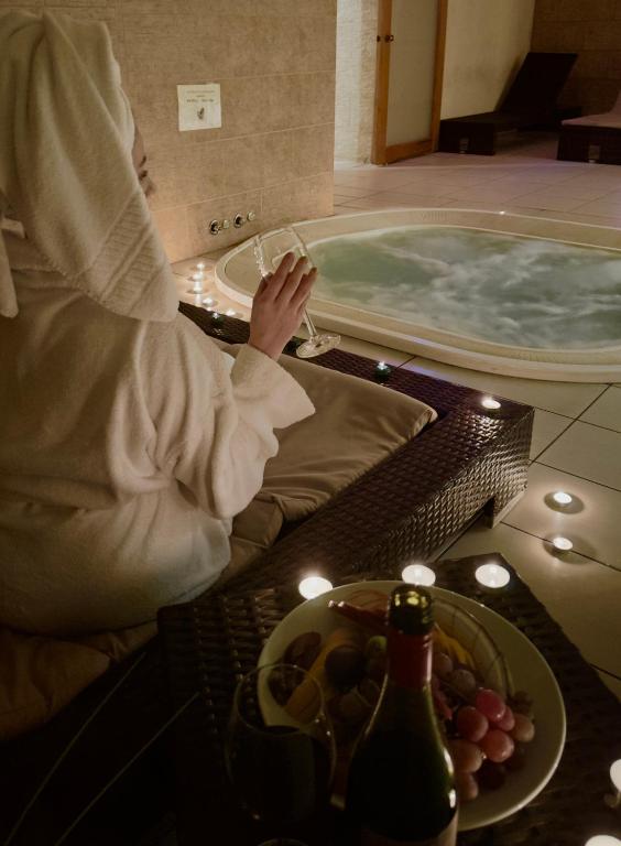 Person in robe holding champagne near candlelit indoor hot tub, intimate spa atmosphere.