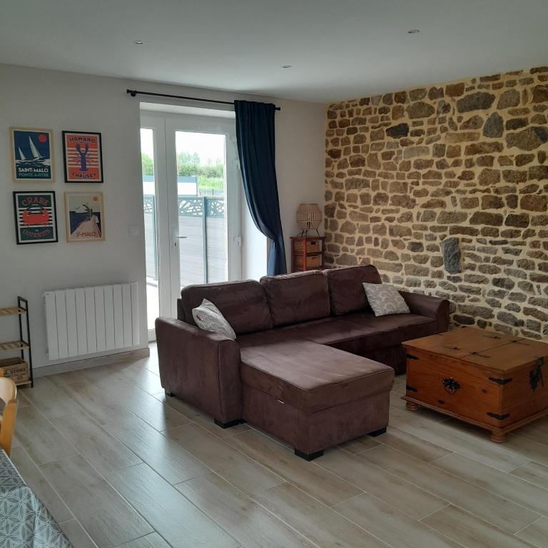 - un salon avec un canapé brun et un mur en briques dans l'établissement La Grange aux Abeilles 2, à Saint-Senier-sous-Avranches