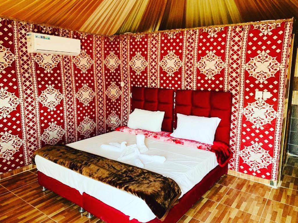 un lit dans une chambre avec un mur rouge dans l'établissement Faiesal Luxury camp & Tour, à Wadi Rum