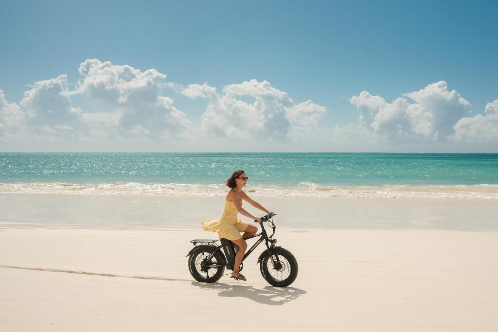 a woman in a yellow dress riding a bike on the beach at Zanzibar White Sand Luxury Villas & Spa - Relais & Chateaux in Paje