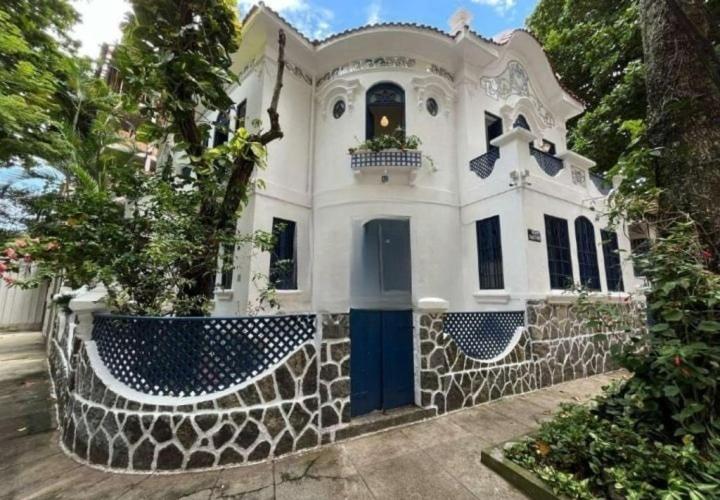 a white house with a blue door and a fence at Casa Colonial 3 Suites na Urca - Rio de Janeiro, Vista Baía Guanabara e Vista Pão de Açucar in Rio de Janeiro