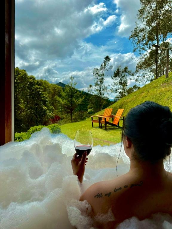 a woman sitting in a bath tub holding a glass of wine at Chalés Brisa Da Montanha in Sapucaí-Mirim