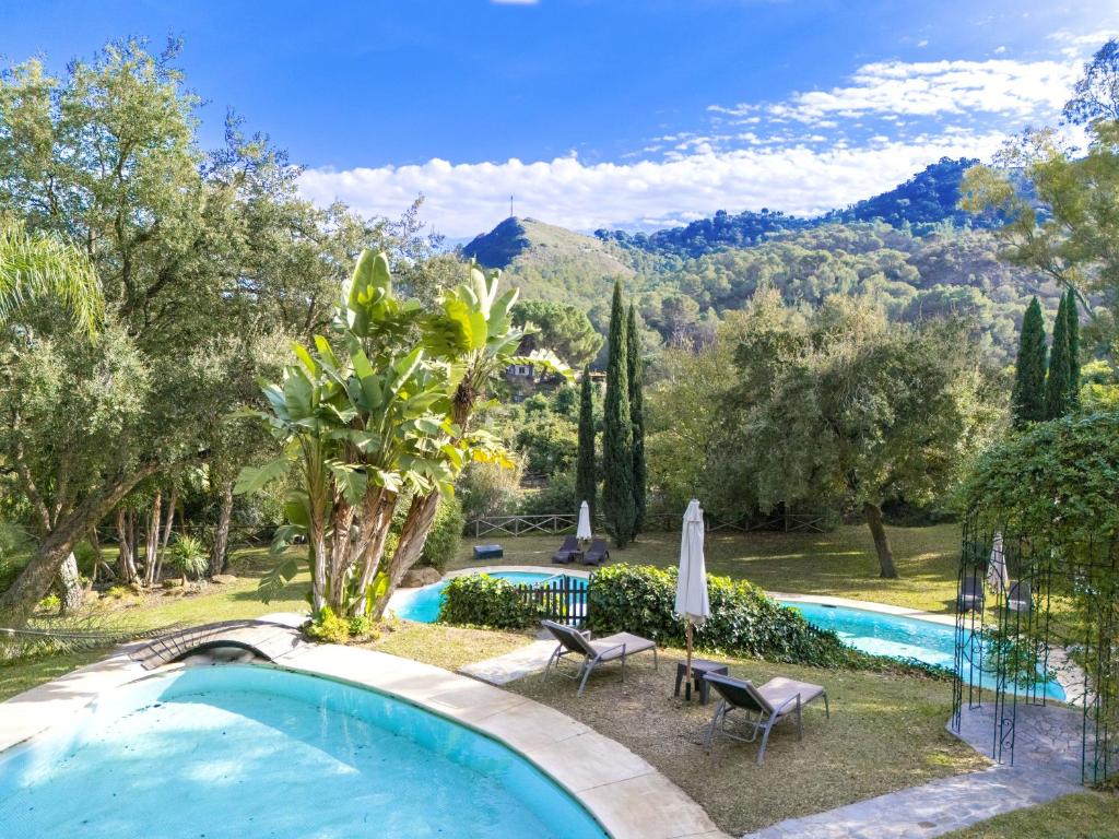 a pool with chairs and umbrellas in a garden at La Fuente del Pedregal Casa 1 - Lago y piscinas in Málaga