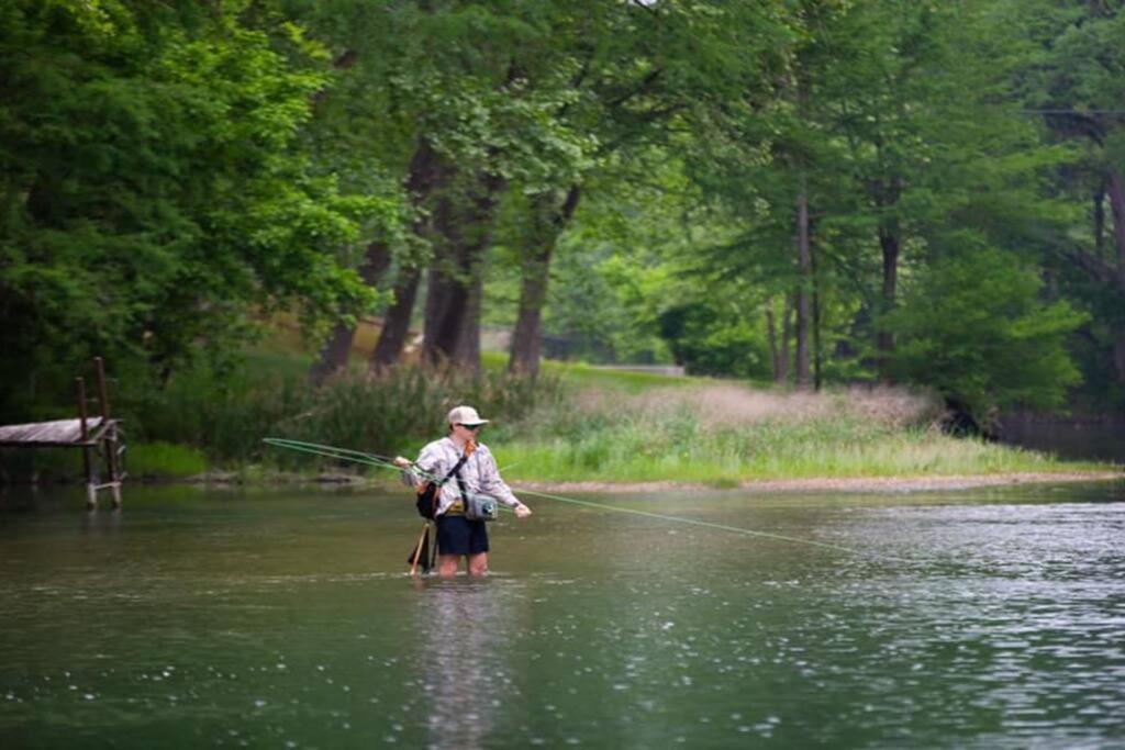 a man standing in a river holding a fishing rod at Treehouse 1 Mockingbird Lodge in New Braunfels